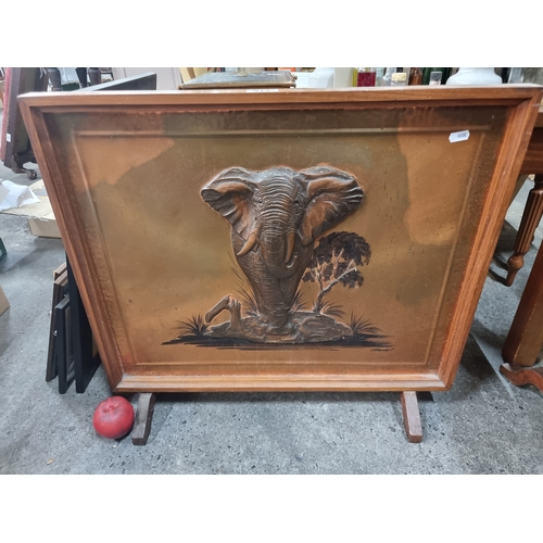 811 - A Dennis Thompson fire screen made in the 1970's featuring a proud African elephant in relief to cen... 