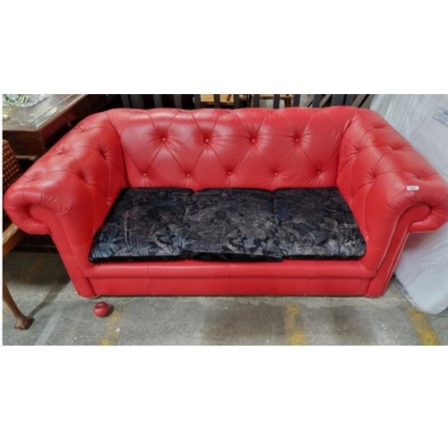 975 - A striking Chesterfield style sofa upholstered in a red button back leather with a trio of midnight ... 