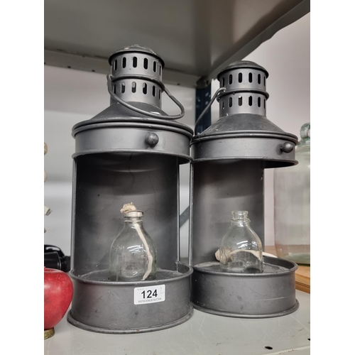 124 - A pair of large metal oil lamp lanterns with glass bottles, fitted with rope.