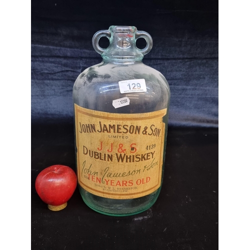 129 - An antique demijohn glass bottle with a label advertising Jameson Dublin Whiskey. In very good condi... 