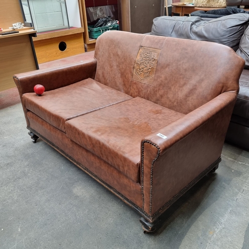 942 - A fantastic two seater sofa upholstered in a brown leather tan with additional lion coat of arms to ... 