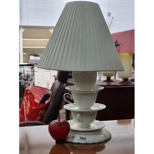 969 - An unusual fun table lamp with a base crafted from teacups and saucers. Topped with a pleated white ... 