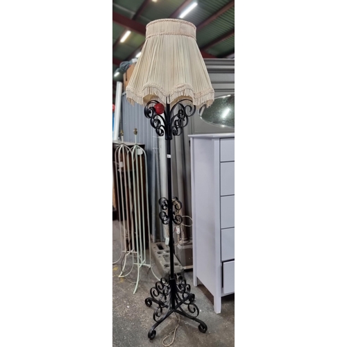 764 - A lovely tall wrought iron floor lamp with stroll detail and an elaborate shade. Fitted with a three... 