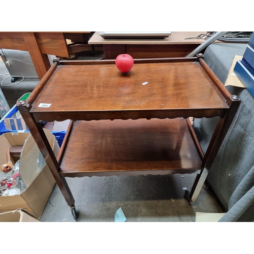 392 - An elegant vintage mahogany drinks cart with two tiers featuring lovely carved aprons. Held on rolli... 