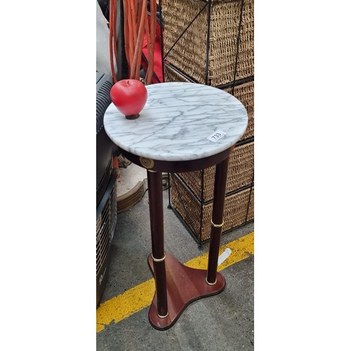 An elegant wooden plant stand with brass features and a marble top.