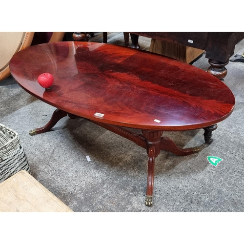 709 - A striking large oval coffee table with brass lion paw feet with a red mahogany finish.