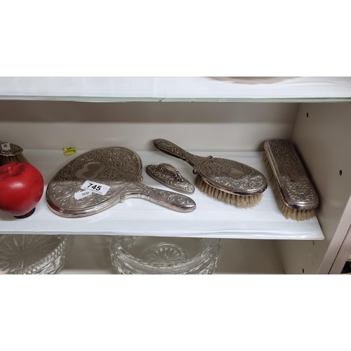 745 - Four silver plate items comprising of a vanity mirror and brushes.