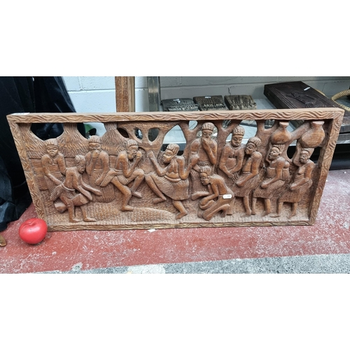 833 - A large hand carved African wooden wall plaque featuring a lively scene of figures dancing, singing ... 