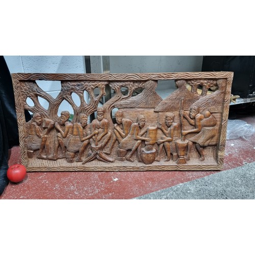 869 - A large heavy African carved wood panel depicting traditional scenes.