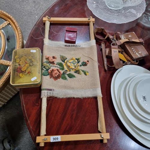 909 - Four vintage items including a wooden embroidery frame with floral panel, a tin containing a large c... 