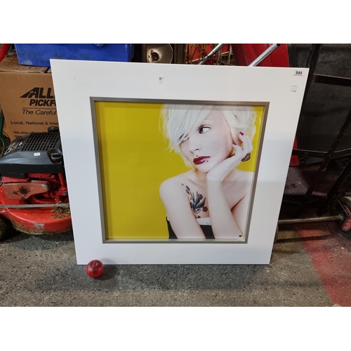 A large good quality photograph depicting a blond model with a vibrant yellow background. Housed in a contemporary white and chrome frame.