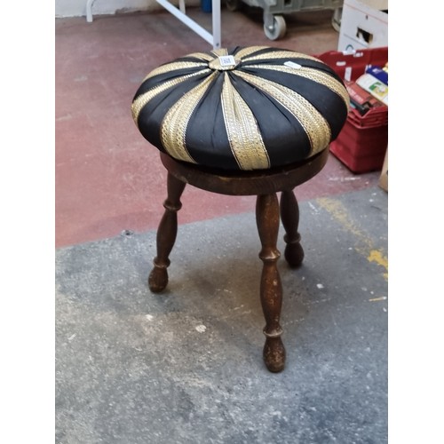 708 - A well made stool with three turned legs accompanied by an ornate gold and black seat cushion.