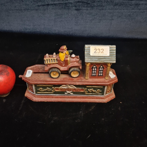 232 - A cheerful cast iron articulated money box in the form of a fire station and a fireman in a truck wh... 