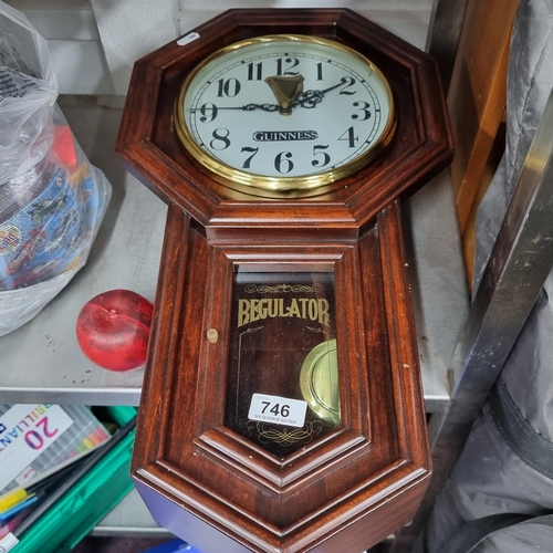 746 - A Guinness branded wall clock held in a handsome wooden frame. Featuring a pendulum, glass and brass... 