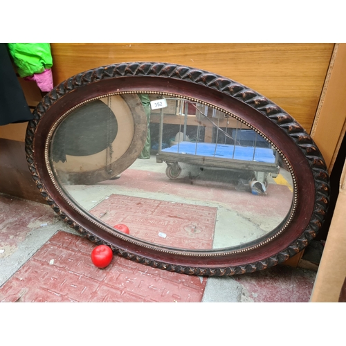 352 - Ornate Victorian-style oval mirror, featuring a braided mahogany frame with rich patina, perfect for... 