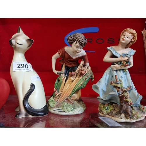 296 - A trio of porcelain figures including an Italian Capodimonte girl example, a Siamese cat and a young... 