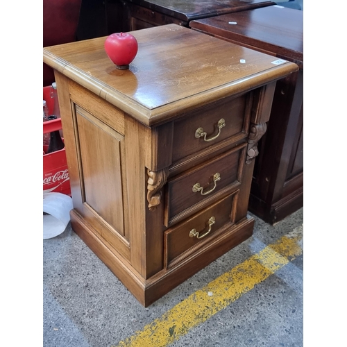 572 - A beautiful well made hardwood bed side locker. Featuring three drawers and brass drop leaf handles.