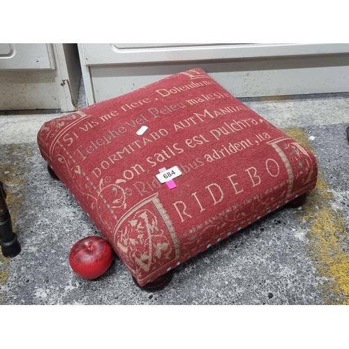 684 - A footstool featuring red upholstery and wooden bun feet.