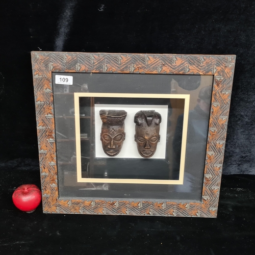 109 - Two fabulous carved wooden African heads. Housed in a deep box frame behind glass.