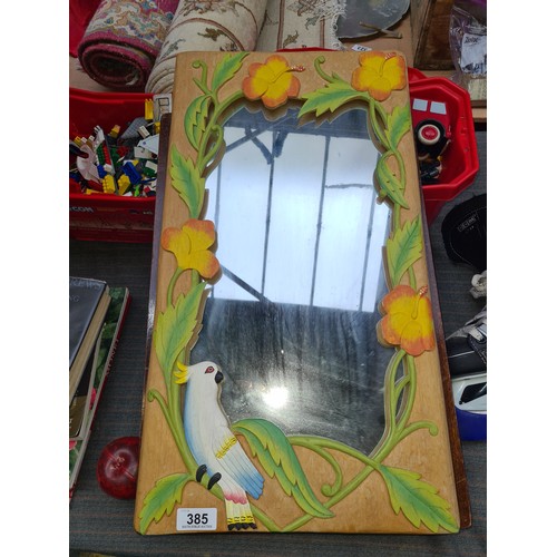 385 - A heavy carved and painted solid wood wall mirror with colourful flower and parrot design.