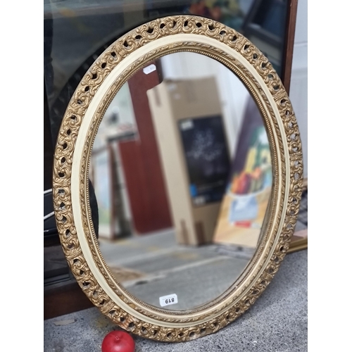 819 - A very heavy and ornate oval wall mirror with thick glass, held in a finely moulded gilt frame.