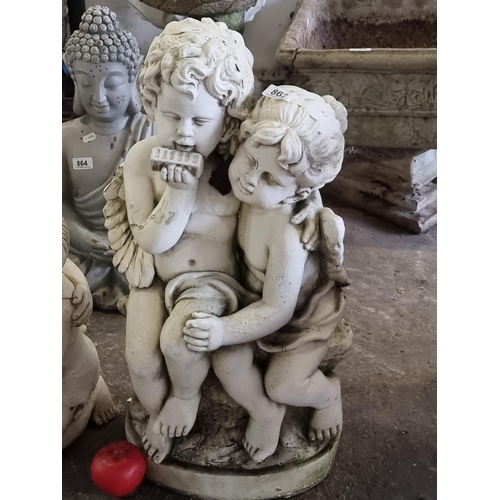 862 - A charming and heavy reconstituted stone garden sculpture of a pair of cherubs embracing, one playin... 