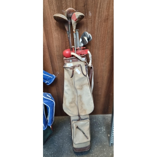 278 - A charming antique canvas golf bag with a number of clubs including some antique wooden examples.