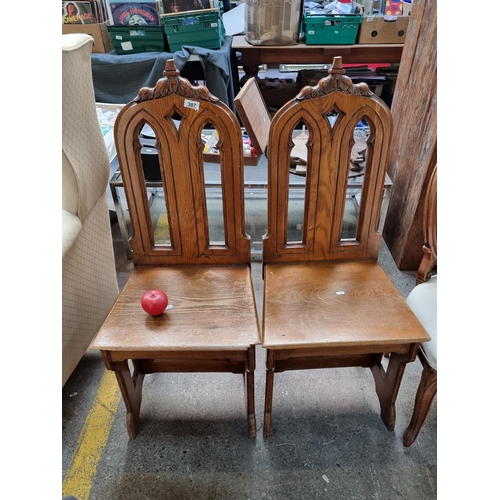 387 - A pair of gothic steeple back solid wood carved hall chairs featuring carved details throughout.