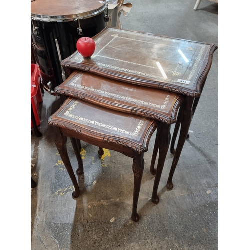 411 - A lovely set of 3 nesting tables boasting tooled leather tops, glass protectors and ornately carved ... 