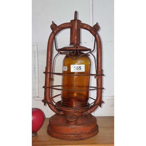 565 - An antique storm oil lantern featuring an orange glass shade.