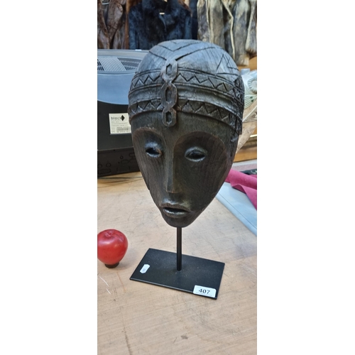 407 - A heavy example of a hand carved wooden African tribal mask depicting a mask. Held on a metal stand.