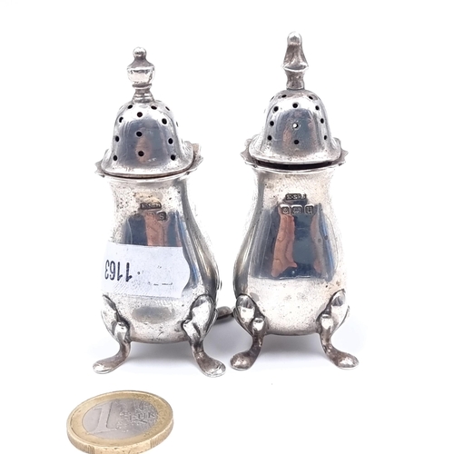 Two sterling silver pepperettes standing on four paw feet, hallmarked Birmingham, height 8cm, set with finial tops. Total weight 55 grams.