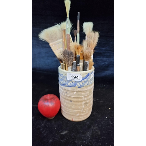 194 - A handcrafted pottery vase containing a large number of various sized artist paintbrushes.