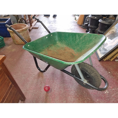 976 - A green wheelbarrow, with a sturdy metal frame and rubber tire, perfect for garden enthusiasts.