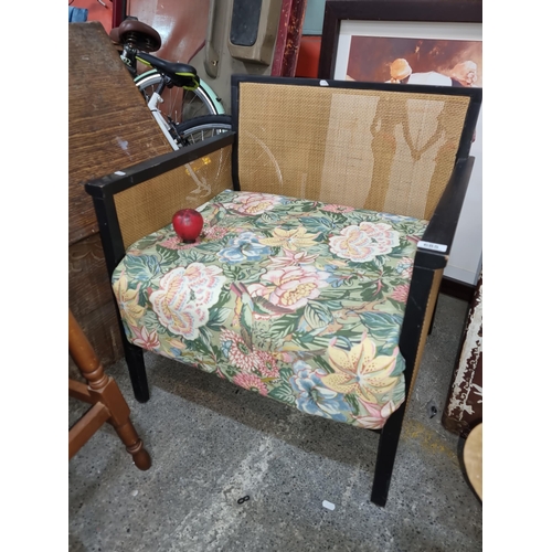 685 - A vintage armchair with upholstered floral pattern seat, sturdy black wooden frame and rattan back a... 