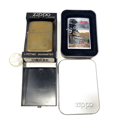 578 - Two unused Zippo lighters. The first a brass foliette design example with a blank cartouche together... 