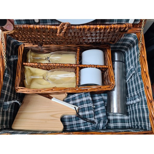 828 - A large wicker picnic basket with leather clasps and handle, containing champagne flutes, mugs, a th... 