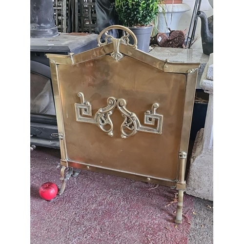 879 - A charming vintage brass fire screen with intricate scrollwork and handle.