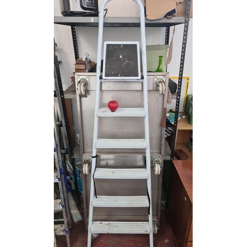 940 - A tall White five-step ladder with a sturdy frame.