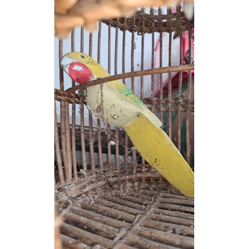 949 - Vintage wicker birdcage with a hand-painted wooden parrot; a charming decorative piece.