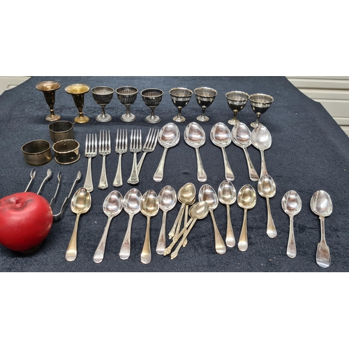 199 - An assortment of egg cups, cutlery, napkin rings and brass candle stick holders. Including some EPNS... 