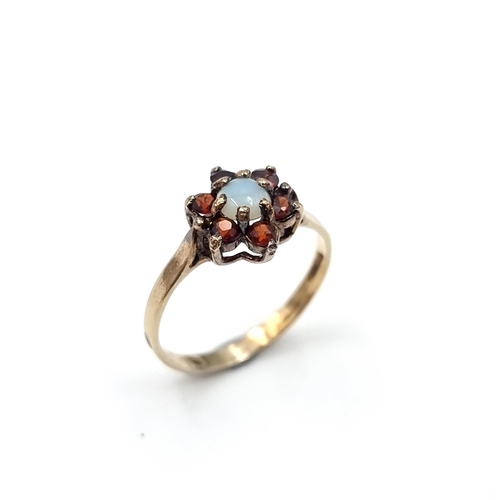 60 - A 9ct gold ring. Set with an Opal and garnet stone surround. Ring size - J. Weight - 1.21 grams.