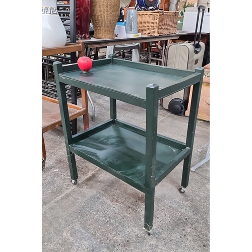 690 - A green painted wooden trolley with two shelves and four casters.