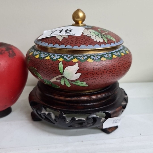 716 - A decorative cloisonné lidded bowl on a carved wooden stand, featuring floral motifs and a blue enam... 