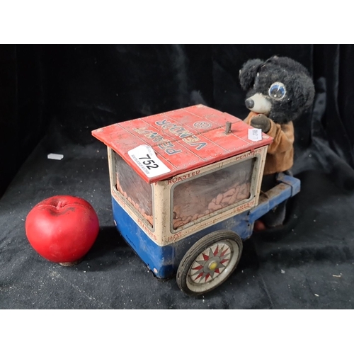 752 - A vintage tin wind-up toy featuring a peanut vendor with dog figure. Mechanical components including... 