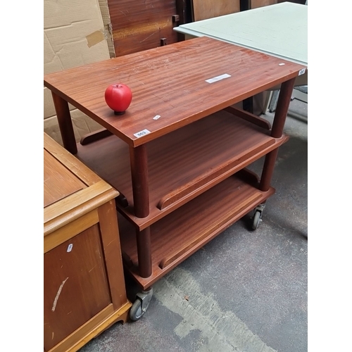 863 - A Mid-Century modern mahogany three-tier shelving unit on caster wheels, featuring a minimalist desi... 