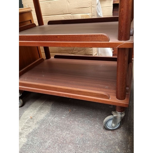 863 - A Mid-Century modern mahogany three-tier shelving unit on caster wheels, featuring a minimalist desi... 