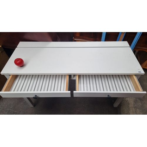 865 - A solid white wooden desk with two drawers, featuring black knobs and striped patterned drawer inter... 