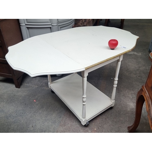 879 - A white-painted drop-leaf side table with turned legs and lower shelf, featuring casters for easy mo... 