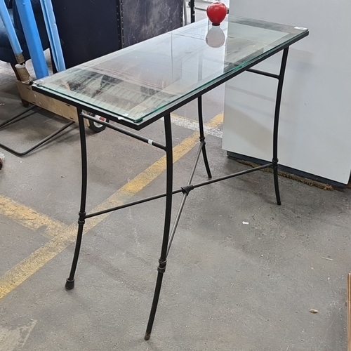 982 - Glass-top console table with slender metal frame, featuring curved supports and cross-bracing for ad... 